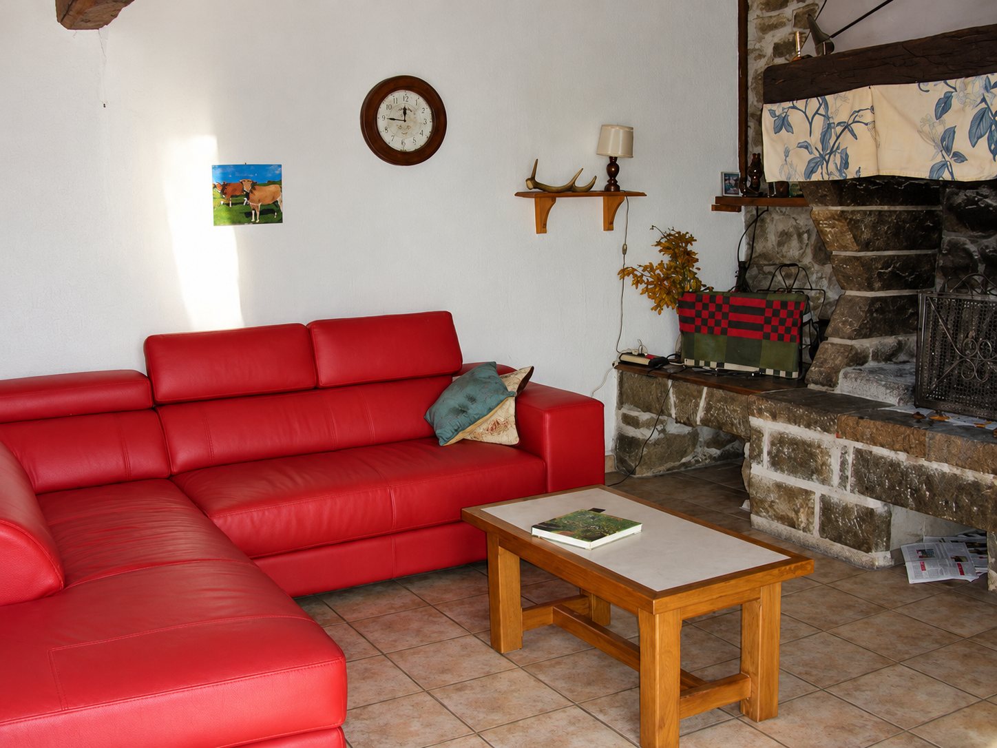 Salon avec un canapé d'angle en cuir rouge, une table basse en bois et une grande cheminée en pierre.